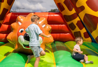 Twee kinderen amuseren zich op een kleurrijk springkasteel met leeuw bij Camping Kost Ar Moor, Bretagne.
