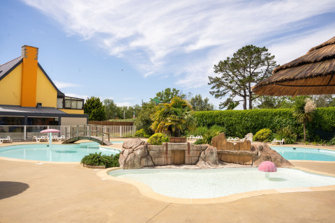 Piscina al aire libre con temática tropical en Camping Kost Ar Moor, parque de vacaciones en Bretaña, Francia.
