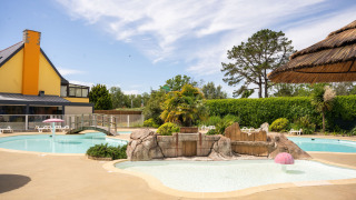Piscina al aire libre con temática tropical en Camping Kost Ar Moor, parque de vacaciones en Bretaña, Francia.