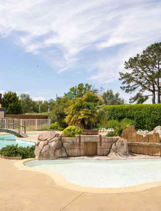 Piscina al aire libre con temática tropical en Camping Kost Ar Moor, parque de vacaciones en Bretaña, Francia.
