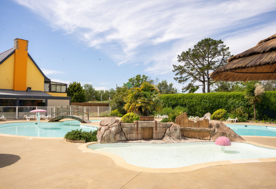 Piscina al aire libre con temática tropical en Camping Kost Ar Moor, parque de vacaciones en Bretaña, Francia.