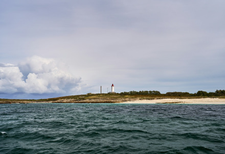 Paisaje costero cerca de Mousterlin - Fouesnant, Bretaña, Francia, con un faro, playa de arena y mar agitado.