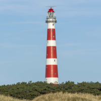 Faro rojo y blanco cerca de Nes, Friesland, Países Bajos, rodeado de dunas y vegetación bajo un cielo despejado.