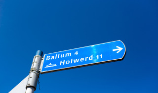 Señal vial hacia Ballum y Holwerd cerca de Nes, Frisia, Países Bajos, bajo un cielo azul claro.
