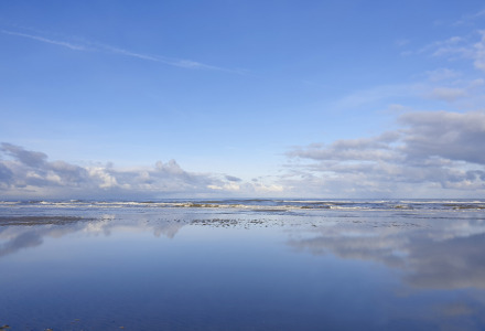 Playa tranquila y mar cerca de Nes, Frisia, Países Bajos, con cielo azul y aguas poco profundas reflectantes.