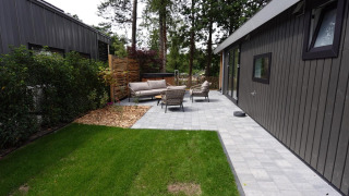Moderne Eco Cottage met terras, zitmeubels en hottub in een groene tuin met bomen.