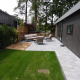 Moderne Eco Cottage med terrasse, havemøbler og spabad i grøn have omgivet af træer.