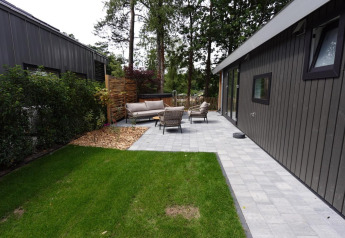 Moderne Eco Cottage med terrasse, havemøbler og spabad i grøn have omgivet af træer.