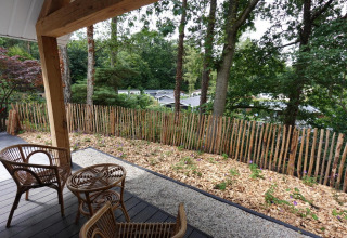 View from Eco Cottage at De Thijmse Berg, Netherlands, featuring rattan chairs, wooden fence, and trees.