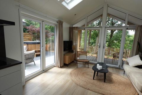 Salón luminoso en Eco Cottage de De Thijmse Berg, Países Bajos, con grandes ventanales, terraza y jacuzzi exterior.