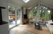 Lys stue i Eco Cottage ved De Thijmse Berg, Holland, med store vinduer, terrasse og spabad udenfor.