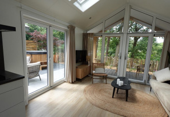Lys stue i Eco Cottage ved De Thijmse Berg, Holland, med store vinduer, terrasse og spabad udenfor.