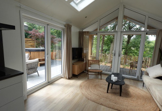 Bright living room in Eco Cottage at De Thijmse Berg, Netherlands, with large windows, patio, and outdoor hot tub.