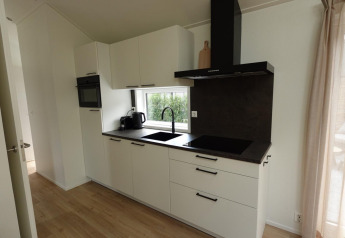 Moderne køkken i Eco Cottage på De Thijmse Berg, Holland, med hvide skabe, sort bordplade og vindue.