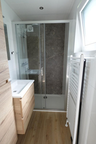 Cuarto de baño moderno con ducha, suelo de madera, toallero y ventana en una cabaña ecológica en Países Bajos.