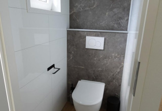 Modern toilet in Eco Cottage + hot tub bij De Thijmse Berg in Nederland met houtvloer en grijze tegelwand.