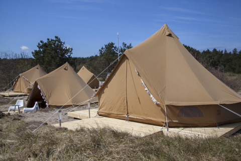 Varios tipis Bell Escape sobre plataformas de madera en la naturaleza, con sillas bajo el cielo azul.
