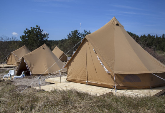 Meerdere Bell Escape tipi tenten op houten vlonders in de natuur, met strandstoelen en blauwe lucht.