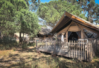 Tenda safari Trapper con veranda in legno tra pini, una persona in piedi all’ingresso della tenda.