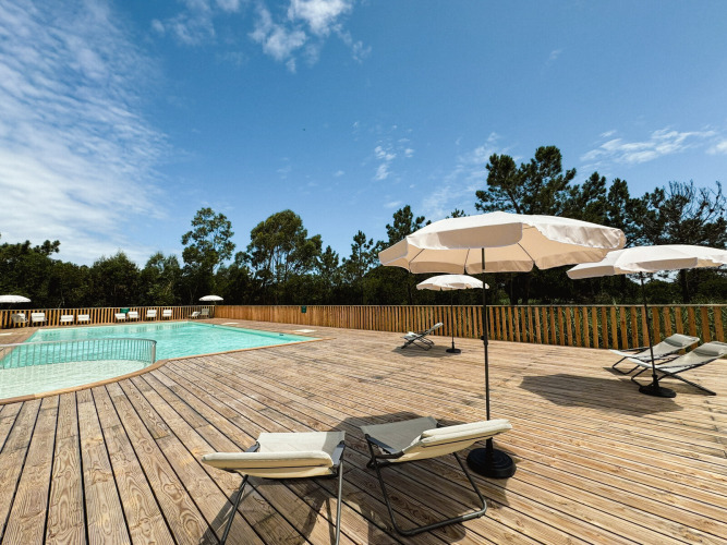 Sunny pool area with lounge chairs and umbrellas on a wooden deck at Village Huttopia Lagoa de Óbidos, Portugal.