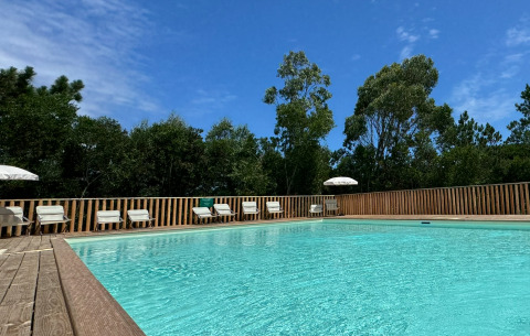 Piscina al aire libre en Village Huttopia Lagoa de Óbidos, rodeada de árboles y tumbonas en Portugal.