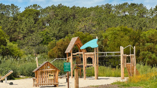 Parque infantil de madera rodeado de vegetación en Village Huttopia Lagoa de Óbidos, Portugal Central.