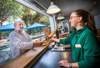En mand modtager et brød fra en medarbejder ved en udendørs café i Village Huttopia Lagoa de Óbidos.