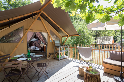 Outdoor deck with dining area and lounging spaces in front of a cozy safari tent called Canadian tent.