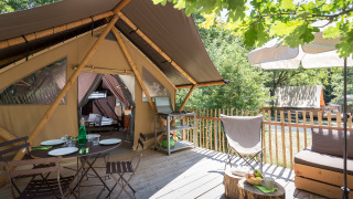 Terraza al aire libre con mesa para cenar y área de descanso frente a una tienda safari llamada Canadian tent.
