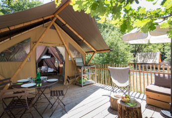 Terraza al aire libre con mesa para cenar y área de descanso frente a una tienda safari llamada Canadian tent.
