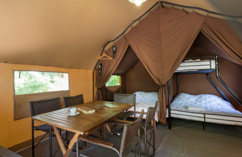 Interieur van een Canadian tent in Village Huttopia Lagoa de Óbidos, Portugal, met tafel, stoelen en bedden.