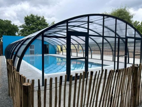 Piscina cubierta con estructura de cristal y valla de madera en Camping Seasonova du Chêne, Pays de la Loire, Francia.