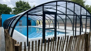 Piscina cubierta con estructura de cristal y valla de madera en Camping Seasonova du Chêne, Pays de la Loire, Francia.