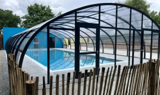 Piscina cubierta con estructura de cristal y valla de madera en Camping Seasonova du Chêne, Pays de la Loire, Francia.