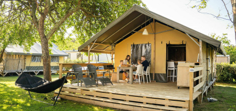 Family dining outside a safari lodge tent at Camping Kost Ar Moor in France, surrounded by lush greenery.
