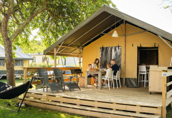 Family dining outside a safari lodge tent at Camping Kost Ar Moor in France, surrounded by lush greenery.