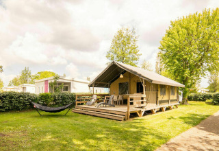 Safari lodge tent at Camping Kost Ar Moor in France, with wooden deck, hammock, and lush green surroundings.
