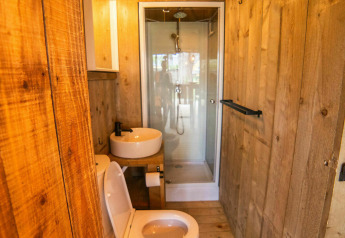 Baño con paredes de madera, inodoro, lavabo y ducha en una tienda Safari Lodge en Camping Kost Ar Moor, Francia.