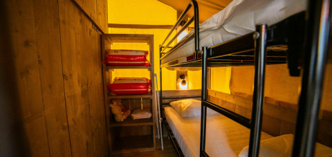 Foto interior de la tienda Safari lodge en Camping Kost Ar Moor, Francia, con literas y estantería visibles.