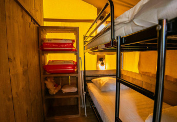 Foto interior de la tienda Safari lodge en Camping Kost Ar Moor, Francia, con literas y estantería visibles.