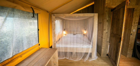 Interior de la tienda Safari Lodge en Camping Kost Ar Moor, Francia, con cama y decoración de madera.