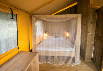 Interior de la tienda Safari Lodge en Camping Kost Ar Moor, Francia, con cama y decoración de madera.