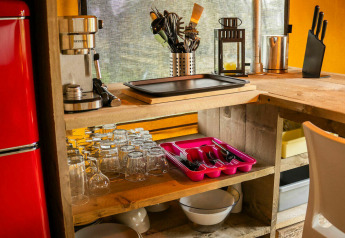 Área de cocina en tienda safari en Camping Kost Ar Moor, Francia, con nevera roja y utensilios de cocina.