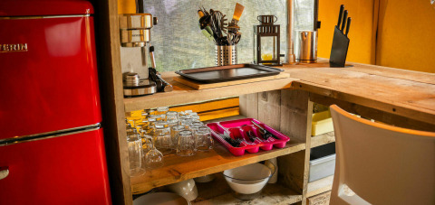 Kitchen area inside a safari tent at Camping Kost Ar Moor, France, showing red fridge and utensils.