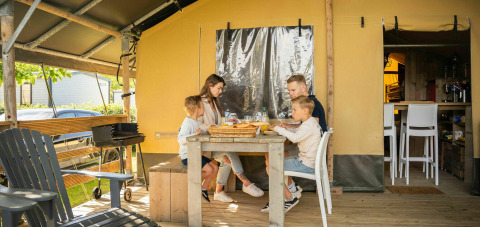 Familia disfrutando de una comida frente a una tienda safari en Camping Kost Ar Moor, Francia.
