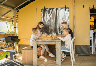 Family dining outside a safari lodge tent at Camping Kost Ar Moor, France, enjoying their meal together.