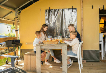 Familia disfrutando de una comida frente a una tienda safari en Camping Kost Ar Moor, Francia.