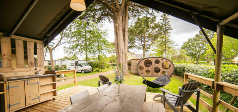 Zicht vanuit de Safari Lodge tent bij Camping Kost Ar Moor in Frankrijk met houten tafel en tuin.