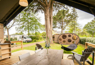 Blick aus dem Safari Lodge-Zelt auf Camping Kost Ar Moor in Frankreich mit Holztisch und grüner Umgebung.