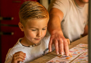 Un niño y un adulto juegan a las cartas juntos en una mesa en una tienda safari en Camping Kost Ar Moor, Francia.